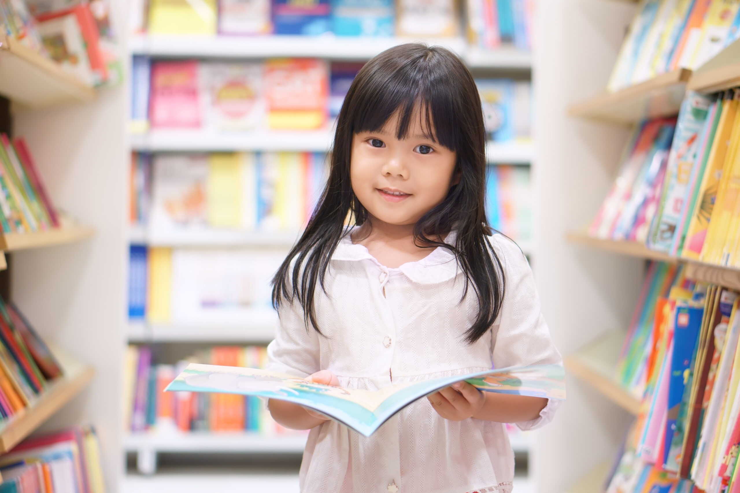 Asian Children Cute or Kid Girl Reading and Choose Tale or Story Book on Bookshelf in Library